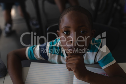 Close-up of black schoolboy with hand on chin sitting at desk and looking at camera in classroom