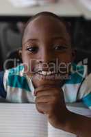 Close-up of black schoolboy with hand on chin sitting at desk and looking at camera in classroom