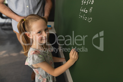 High angle view of schoolgirl writing on chalk board in classroom