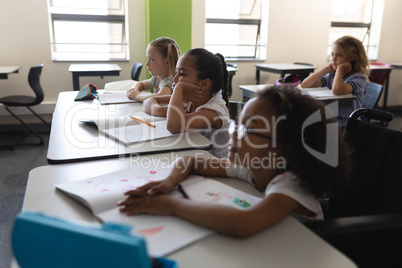 Side view of schoolkids studying and sitting at desk in classroom