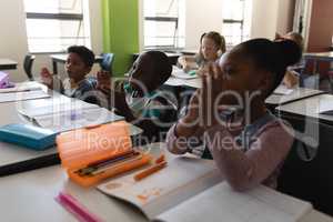 Side view of schoolkids applauding and sitting at desk in classroom