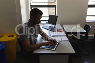 Side view of school teacher working on laptop and sitting at desk in classroom