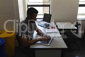 Side view of school teacher working on laptop and sitting at desk in classroom