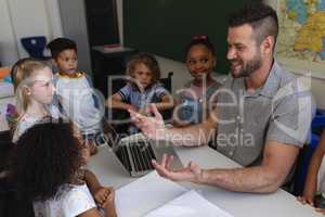 Happy male school teacher teaching schoolkid at desk in classroom