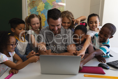 Male school teacher teaching schoolkid on laptop at desk in classroom