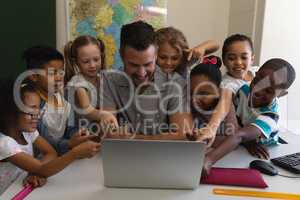Male school teacher teaching schoolkid on laptop at desk in classroom