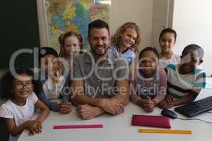 Happy male teacher and schoolkids looking at camera in classroom
