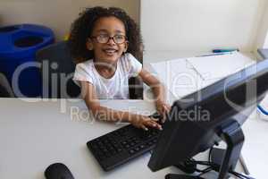 High angle view little schoolgirl using desktop pc at desk in classroom