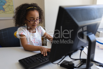 Front view little schoolgirl using desktop pc at desk in classroom