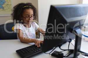 Front view little schoolgirl using desktop pc at desk in classroom