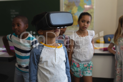 Front view of schoolboy using virtual reality headset in classroom