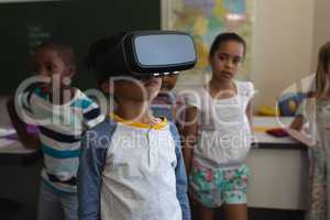 Front view of schoolboy using virtual reality headset in classroom