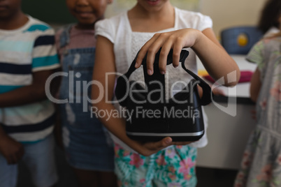 Mid section of schoolgirl holding virtual reality headset in classroom