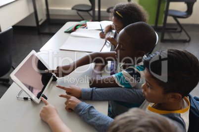 High angle view of schoolkids studying on digital tablet while sitting at desk in classroom
