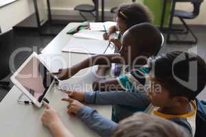 High angle view of schoolkids studying on digital tablet while sitting at desk in classroom