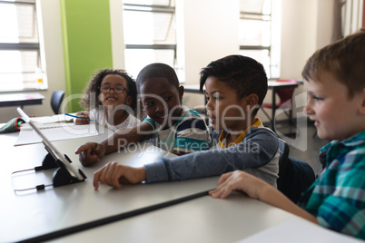 Side view of schoolkids studying on digital tablet while sitting at desk in classroom