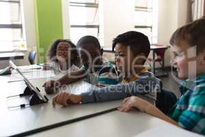 Side view of schoolkids studying on digital tablet while sitting at desk in classroom