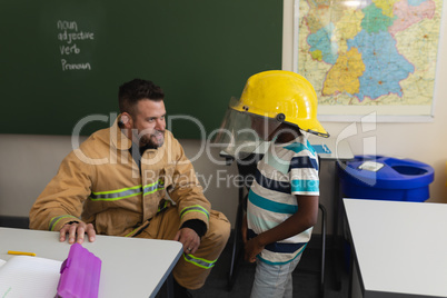 Male firefighter teaching schoolboy about fire safety in classroom
