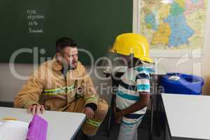 Male firefighter teaching schoolboy about fire safety in classroom