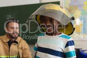 Happy schoolboy wearing fire helmet in classroom