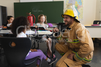 Side view of male firefighter teaching schoolkids about fire safety in classroom