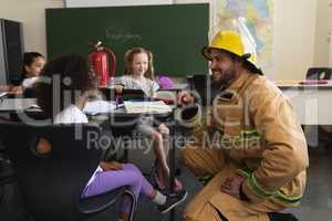 Side view of male firefighter teaching schoolkids about fire safety in classroom
