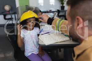 Firefighter wearing helmet to schoolgirl in classroom