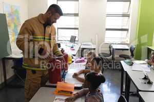 Side view of male Caucasian  firefighter teaching schoolkids about fire safety in classroom