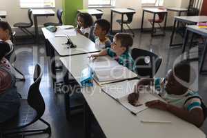 Side view of schoolkids studying and sitting at desk in classroom