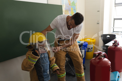 Male firefighter help to wearing fire uniform to schoolgirl in classroom