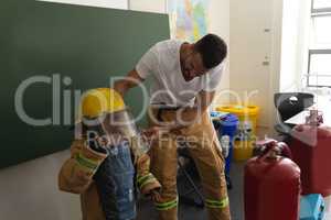 Male firefighter help to wearing fire uniform to schoolgirl in classroom