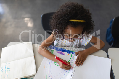 High angle view of schoolgirl drawing in book in classroom