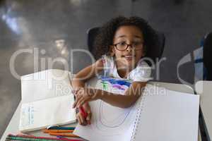 High angle view of schoolgirl drawing in book while looking at camera in classroom
