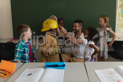 Male firefighter help to wearing fire uniform to schoolkid in classroom