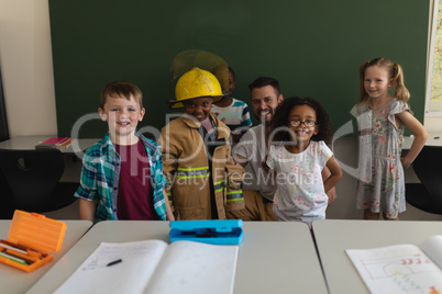 Happy male firefighter with schoolkids looking at camera in classroom