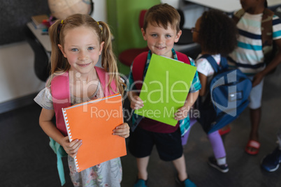 Front view of schoolkid holding notebook and looking at camera in classroom