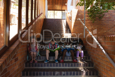 Schoolkids reading book while sitting on stairs of elementary school