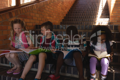 Schoolkids reading book while sitting on stairs of elementary school