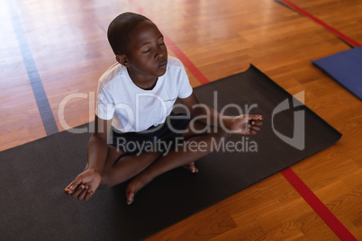 Schoolboy doing yoga and meditating on a yoga mat in school