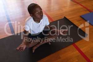 Schoolboy doing yoga and meditating on a yoga mat in school