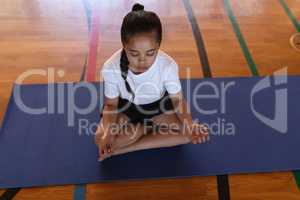 Schoolgirl doing yoga and meditating on a yoga mat in school