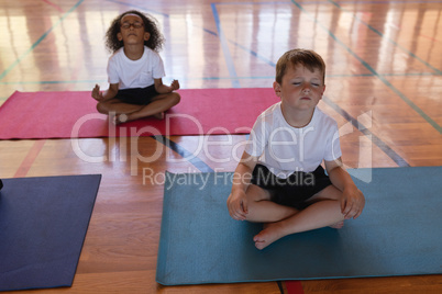 Schoolkids doing yoga and meditating on a yoga mat in school