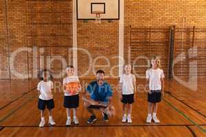 Happy basketball coach and schoolkids looking at camera at basketball court
