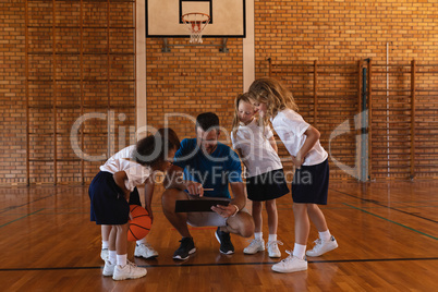 Schoolkids looking at clipboard at basketball court in school