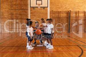 Schoolkids and basketball coach forming hand stack at basketball court in school