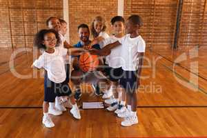 Schoolkids and basketball coach forming hand stack and looking at camera in basketball court
