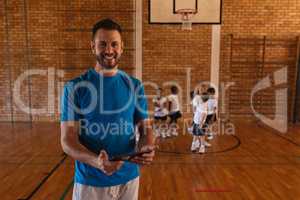 Happy basketball coach using digital tablet at basketball court in school