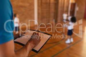 Basketball coach writing on clipboard at basketball court in school