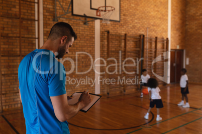 Basketball coach writing on clipboard at basketball court in school
