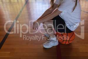 Low section of schoolgirl sitting on basketball at basketball court